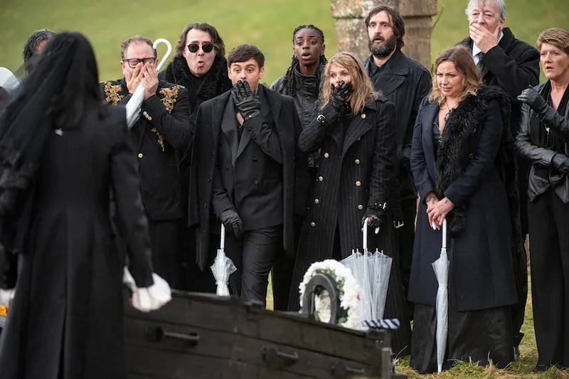 A group of funeral mourners gasp in front of an open coffin