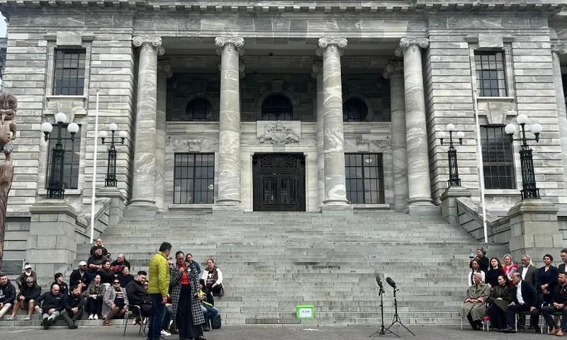 Two crowds sit outside the parliament building, in front of the parliament steps, with a petition box between them.