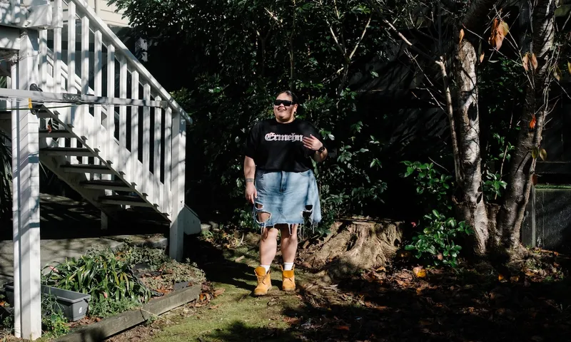 a young woman in a black t-shirt, denim skirt and Timbaland boots stands in her garden wearing dark sunglasses