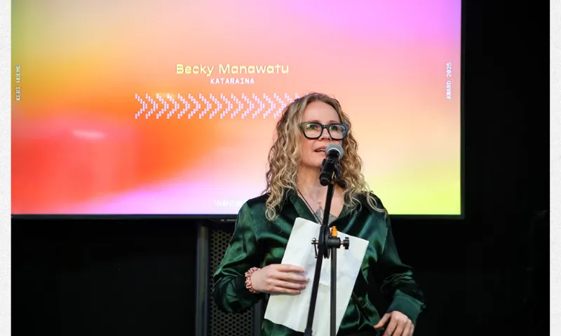 A photo of Becky Manawatu on a stage at a microphone speaking.