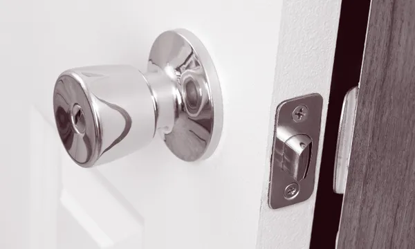 a black and white close up image of a door handle and a door slightly ajar