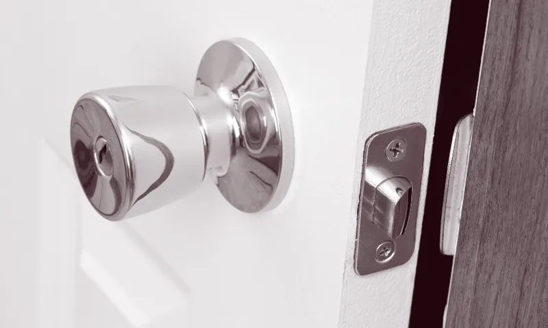 a black and white close up image of a door handle and a door slightly ajar