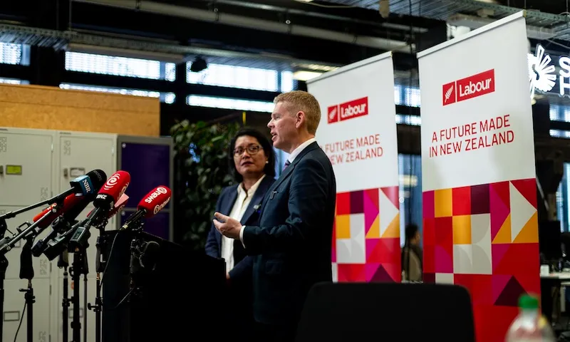 Two people stand at a podium with several microphones, speaking in front of two Labour banners that read "A FUTURE MADE IN NEW ZEALAND," inside a modern indoor setting with bright lighting.