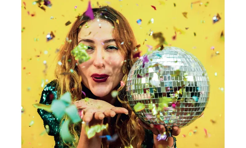A photograph of a women blowing confetti and holding a disco ball.