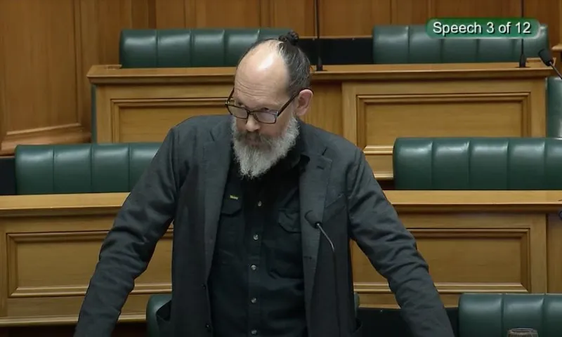 Steve Abel, leaning over his desk, speaks to the House on the MACA bill.