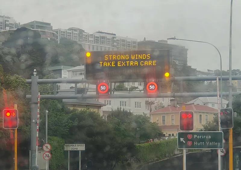 A rainy day in Wellington with a giant sign across motorway reading "STRONG WINDS TAKE EXTRA CARE"