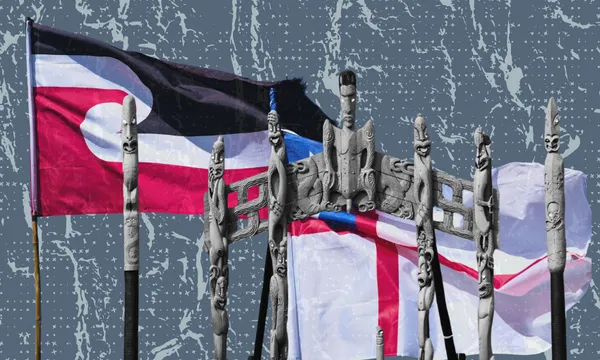 The Tino Rangatiratanga and New Zealand flags wave behind carved Māori wooden figures and a traditional gateway against a patterned blue background.