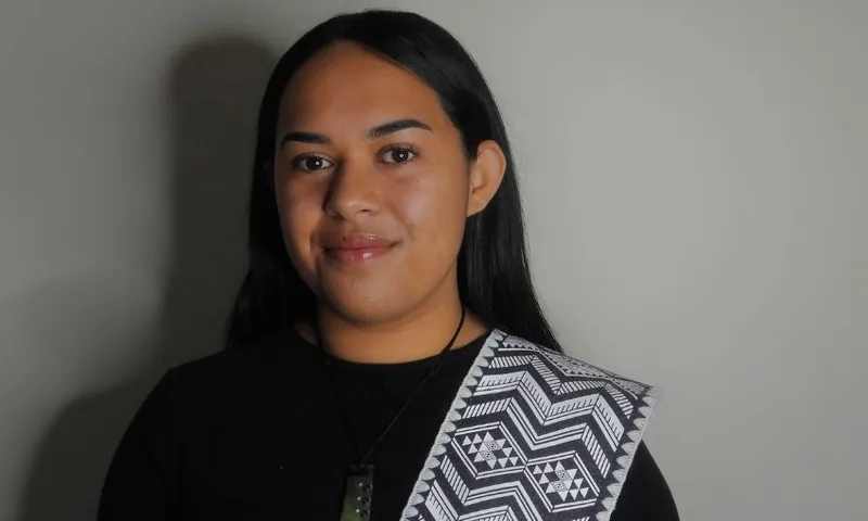 A young wāhine Māori smiles against a plain background.
