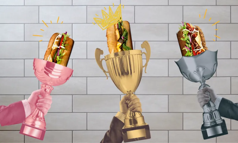 Three hands hold trophies with sandwiches inside: a pink trophy on the left, a gold trophy with a drawn crown in the center, and a silver trophy on the right, all against a tiled wall background.