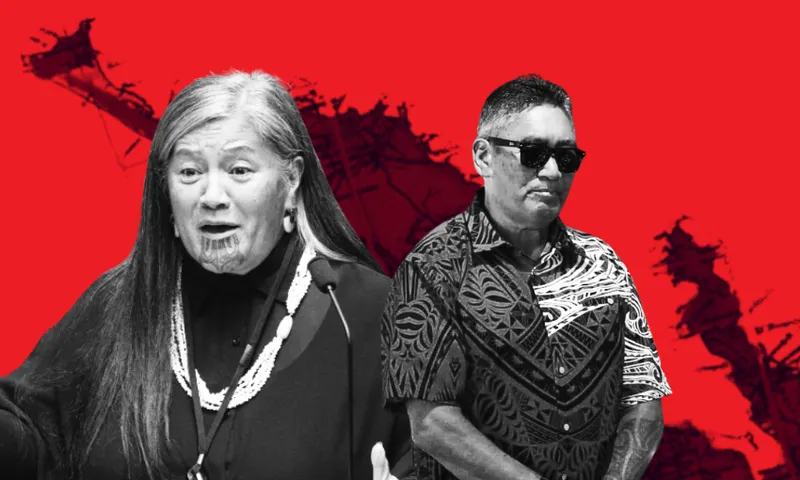A woman with long gray hair speaks at a podium, wearing a necklace, against a red background with a map. Beside her, a man in sunglasses and a patterned shirt stands with folded arms.