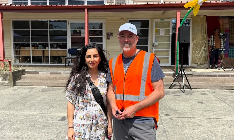 A young woman in a white dress and a man in a high vis vest stand in front of a classroom.