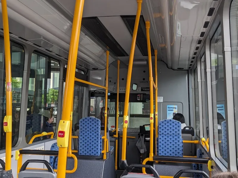 a bus with yellow poles and stop buttons and a small 'coming soon' sign about Motu Move which someone forgot to remove