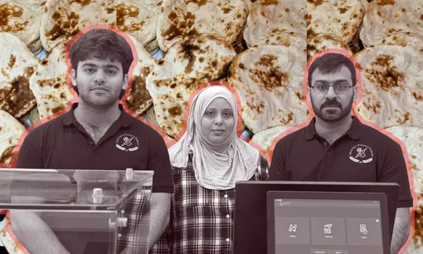 Three people wearing dark shirts and standing behind a counter, with a woman in a headscarf between two men, set against a background filled with flatbread.