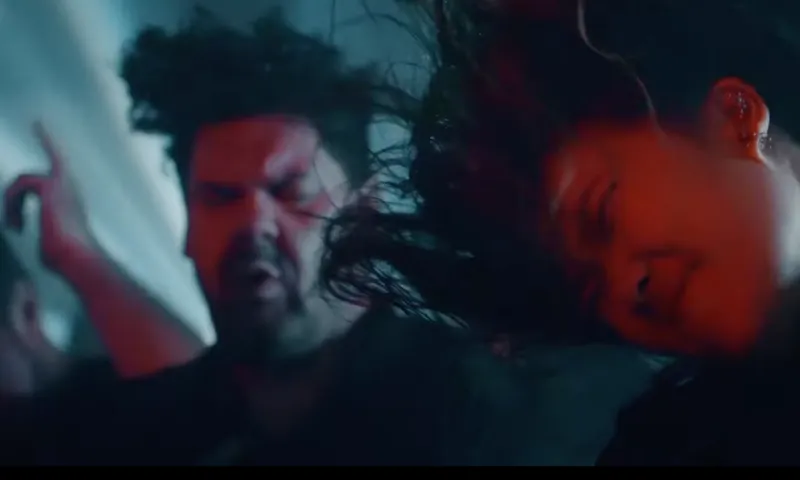 Two people at a concert headbanging with their eyes closed, hair flying, and faces showing intense emotion under dramatic lighting.