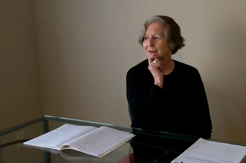 A woman at a table with papers in front of her. She is wearing black and has a short, grey bob.
