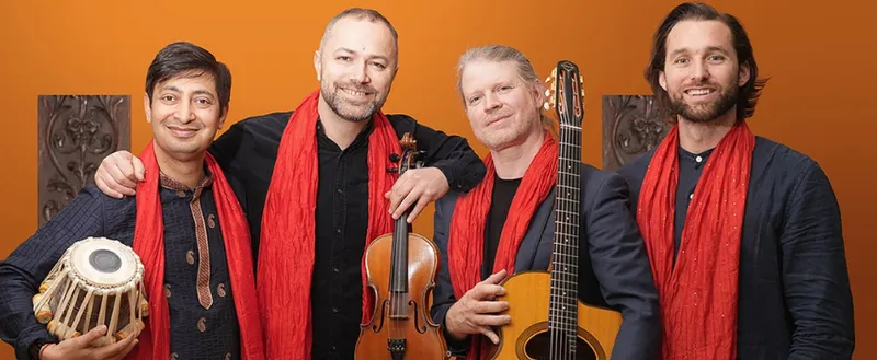 A photo of four men wearing red scarves and holding instruments: they are all smiling.