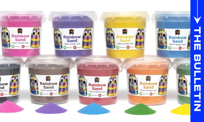 Nine tubs of colorful Rainbow Sand are arranged in two rows, each with a matching pile of sand in front. A blue vertical banner on the right reads "THE BULLETIN" in white text.