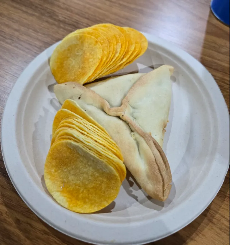 A plate with a stack of potato chips and a folded, triangular baked pastry on a wooden table.
