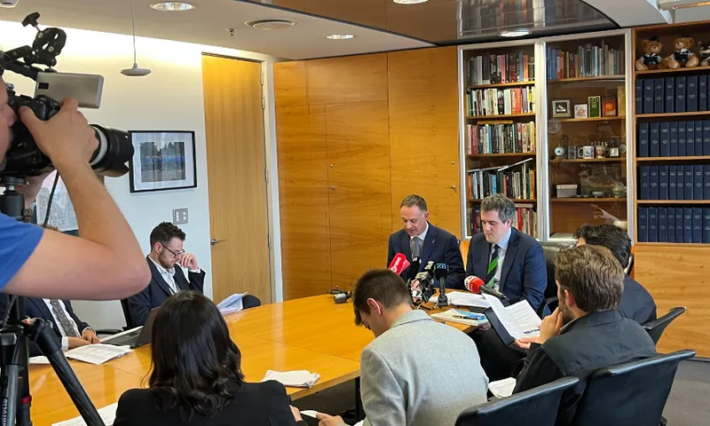Inside Chris Bishop's office, with Bishop and minister Simon Watts sitting at the head of a table filled with journalists.