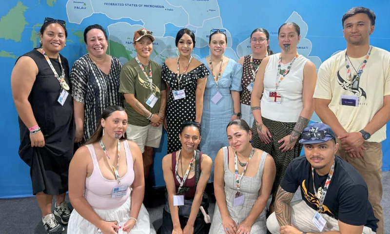 A group of twelve people pose together, some standing and some kneeling, in front of a blue map backdrop. Several women have traditional chin tattoos. All are wearing name badges and smiling at the camera.
