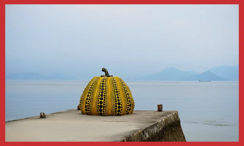 A large yellow pumpkin sculpture with black dots sits at the end of a concrete pier, overlooking calm water with distant blue mountains and a boat in the background. The image has a red border.