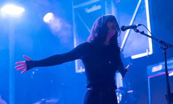 A woman singing into the microphone and holding out her arms wide. The state is blue with lighting.