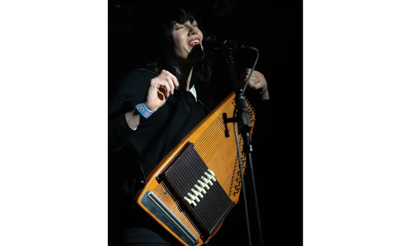 A woman singing into a microphone and holding an autoharp.