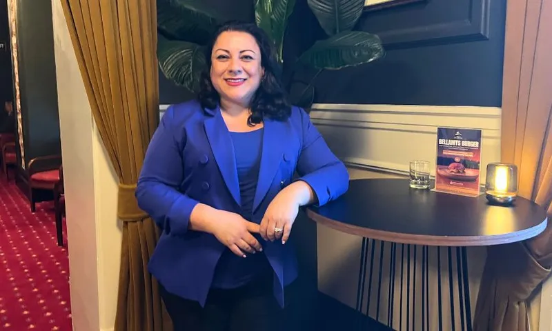 Rima Nakhle, wearing a blue blazer and shirt, leans against a bar table at Pint of Order.