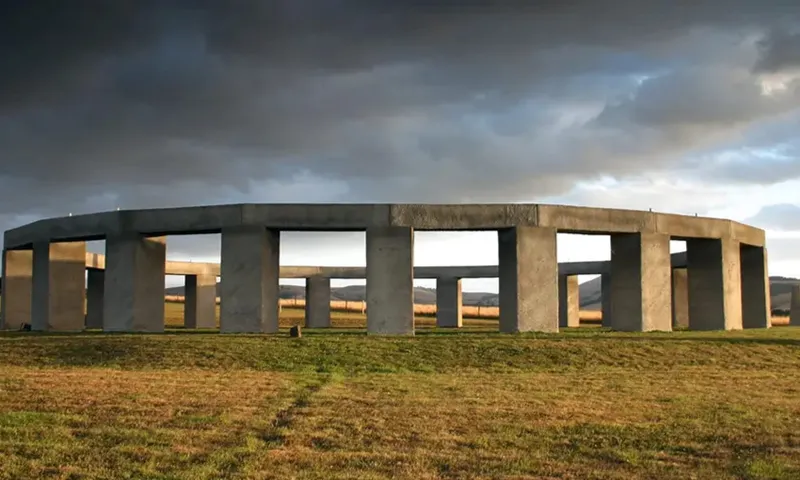 A large outdoor stone sculpture sitting on grass with a gloomy sky above.
