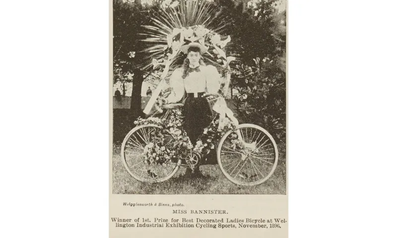 A black and white newspaper clipping showing a woman with a decorated bike.