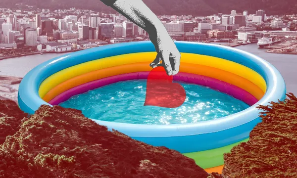 A hand holds a red heart above a colourful inflatable pool filled with water, set against a city skyline and surrounded by green trees.