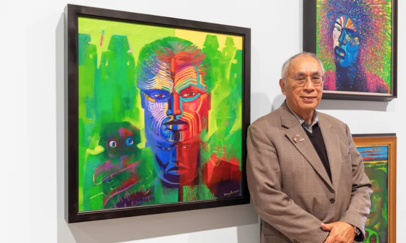 An older man in a brown suit stands beside a colorful, abstract portrait featuring a face with vibrant red, blue, and green hues, displayed in an art gallery. More colorful artwork is visible on the wall behind him.