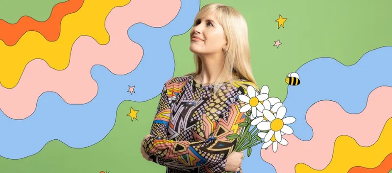 A photo of artist Ruby Jones who is a young woman with blonde hair. She is holding flowers and behind her is a swirly colourful background.