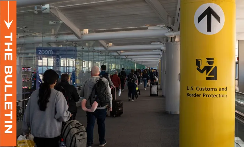 Travelers stand in a line at an airport terminal, waiting near a yellow pillar marked with a U.S. Customs and Border Protection sign. An orange banner on the left reads "THE BULLETIN.