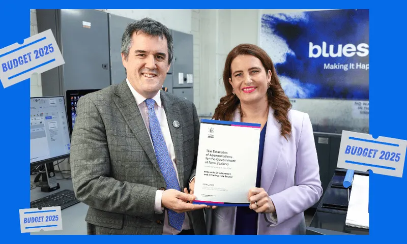 Two people in business attire, Chris Bishop and Nicola Willis, smile while holding an official-looking document. Behind them are office machines and a sign reading "bluesky." Blue "BUDGET 2025" graphics frame the image.