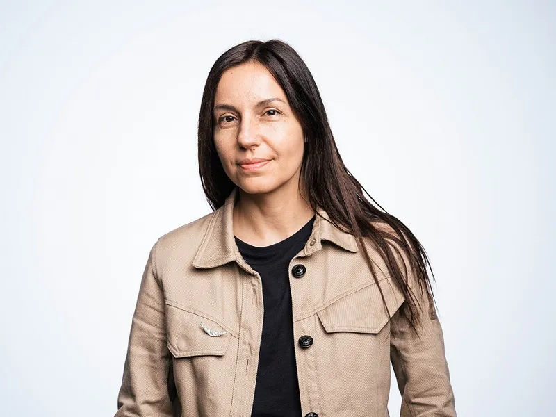 a romanian woman wearing a tan jacket with long brown hair