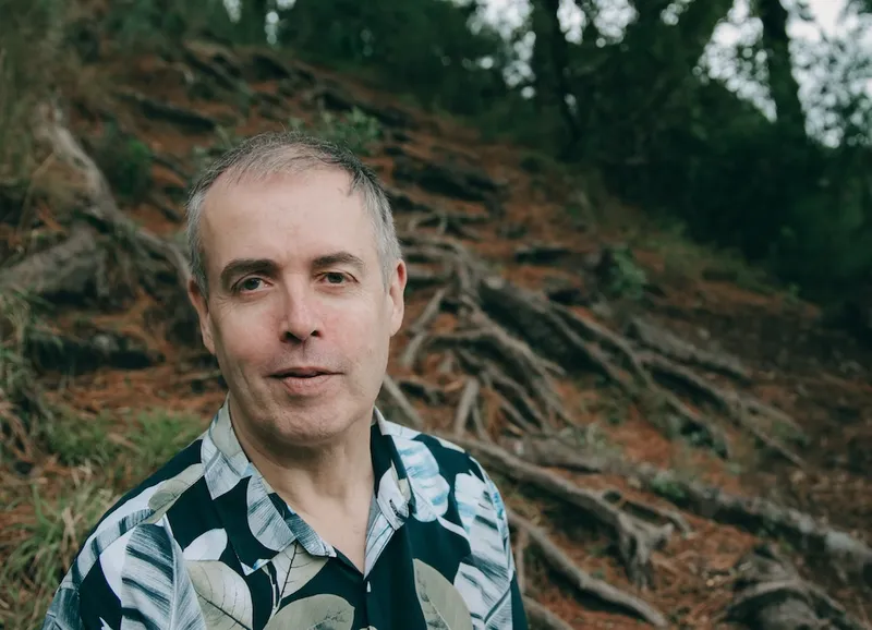 a grey haired man with trees in the background