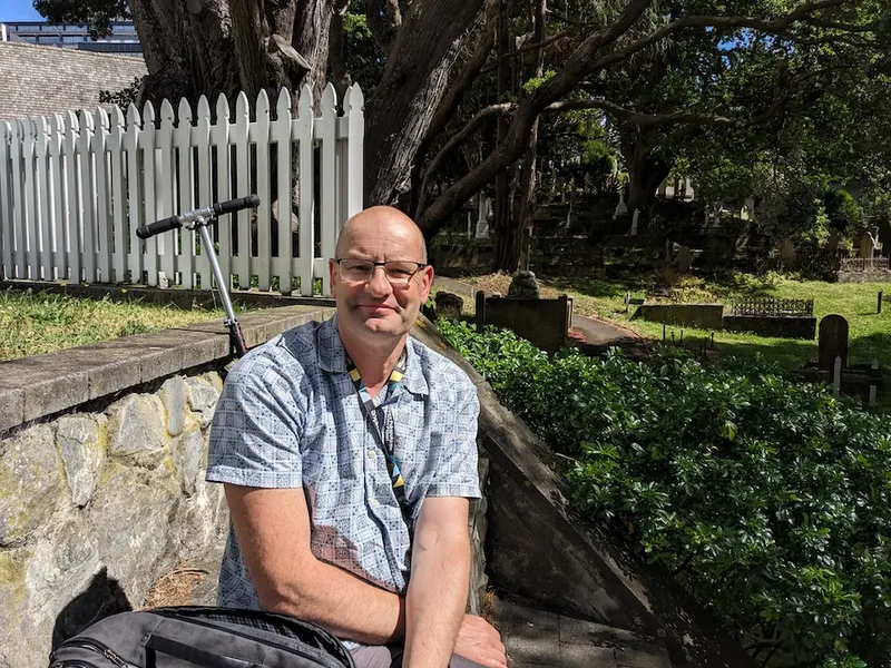 a bald man in a short sleeved shirt in a shady cemetery