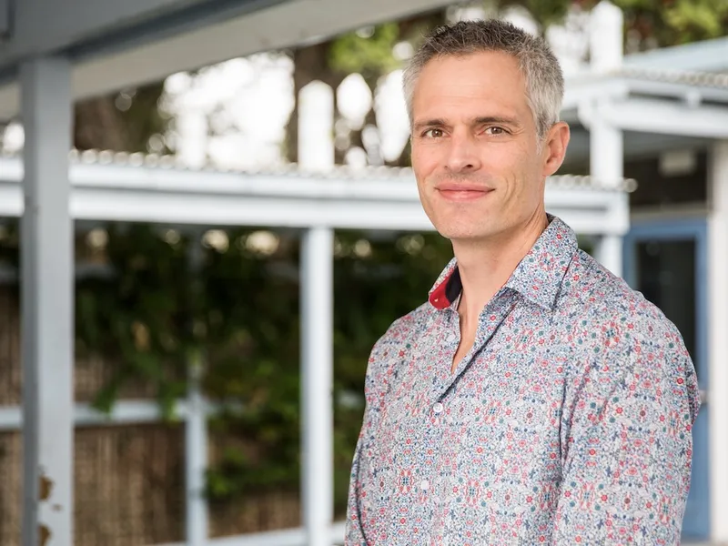 a friendly looking greay haired white man with a colourful shirt and subtle smil looking at the camera