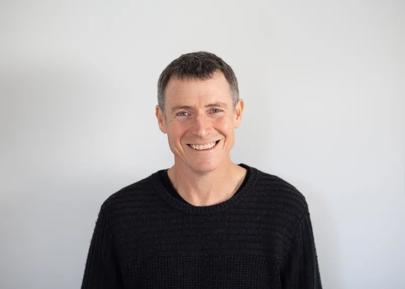 john robertson, a man with close cropped grey hair smilling against a blank background
