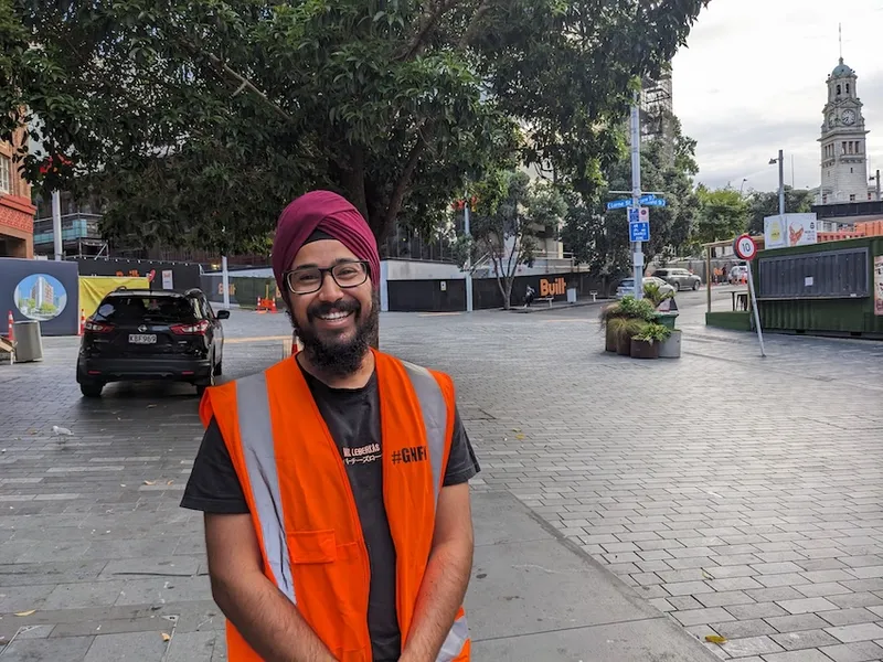 a smiling man in a red turban and orange hi vis vest - he looks kind and approachable