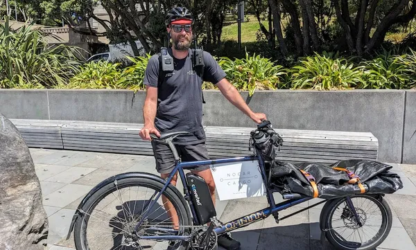 Chris baker, a smiling man with a dark grey tshirt and a helmet holding a long cargo bike
