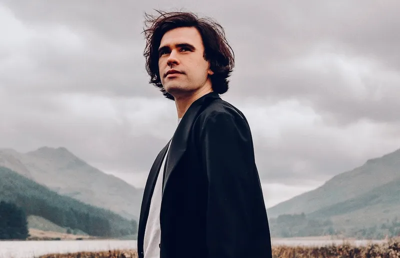 a man with floppy bron hear and the misty scottish mountains behind