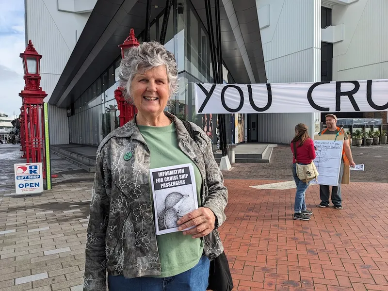 a grey haired woman with a green t-shirt and a smile holding a pamphlet with a picture of a cruise ship and a penguine