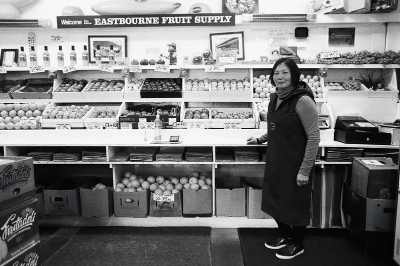 A woman stands in her fruit and vege shop, with goods behind her