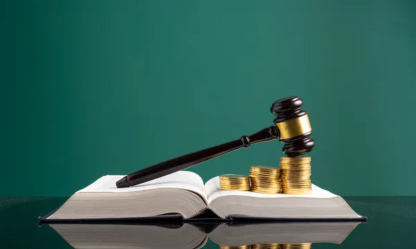 Stack Of Coins With Gavel Over Open Book On Table Against Green Background