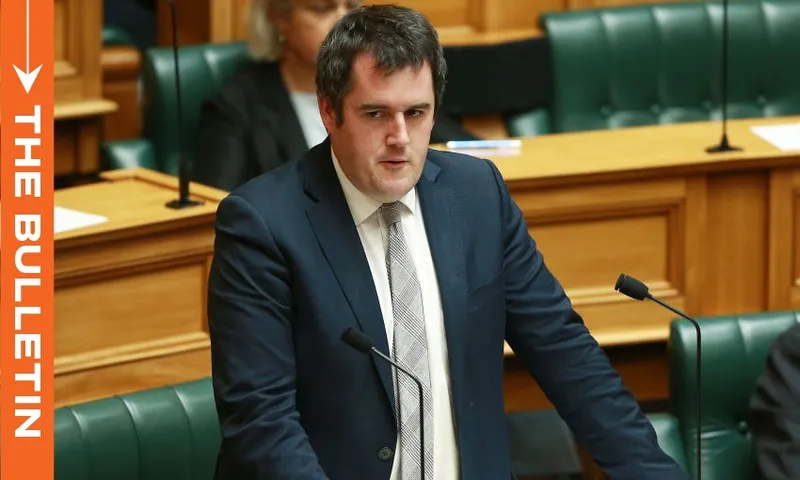 National MP Chris Bishop is speaking in parliament. He is wearing a suit and tie, has short, dark hair, and is looking slightly to the side. The background shows green leather seats and wooden panels, typical of legislative chambers.