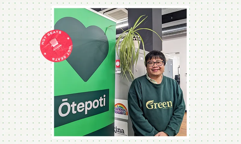 a filipino man in a green sweater staning next to a Green party sign with a plant dangling in his face