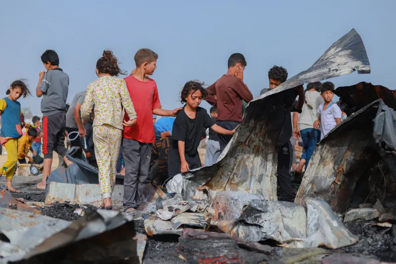 Children gathered around twisted and burnt corrogated iron