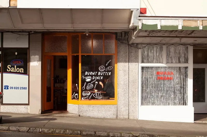 an exterior shot of burnt butter diner with orange window sills and the Moana Fresh arts store next door with a silver glittery curtain